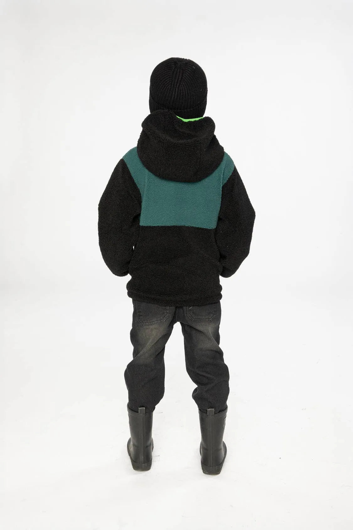 Child seen from behind wearing the jacket's black sherpa side, showing the teal back panel and the hood