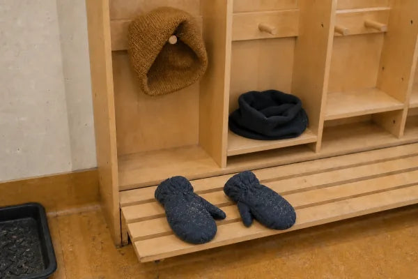 A used pair of mittens, a toque, and a neck warmer rest across daycare cubbies.